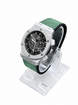 Men's silver skeleton chronograph watch with green leather-style strap and detailed black open-style dial